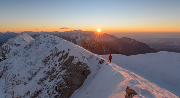 Black mountaineer silhouetted against sunrise on Himalayan peak with Everest visible in background