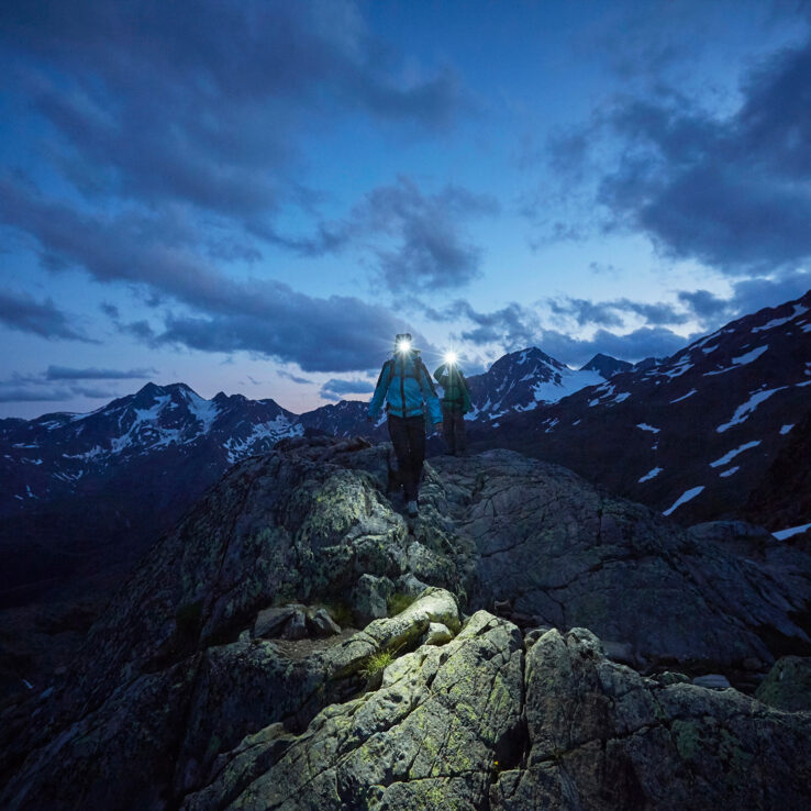 Multiple headtorch beams illuminating dark mountain trail during night hiking challenge