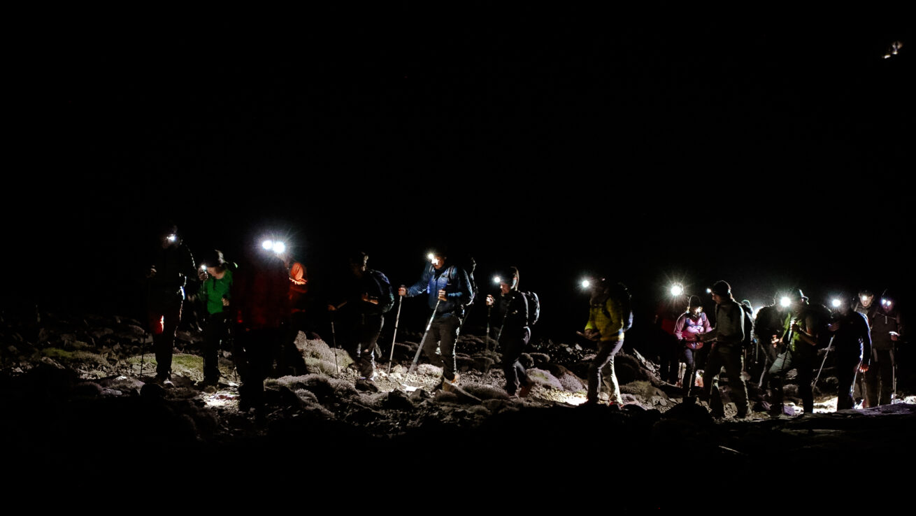 Corporate team celebrating summit success at night on Carrauntoohil with headtorches illuminating Irish mountain peak