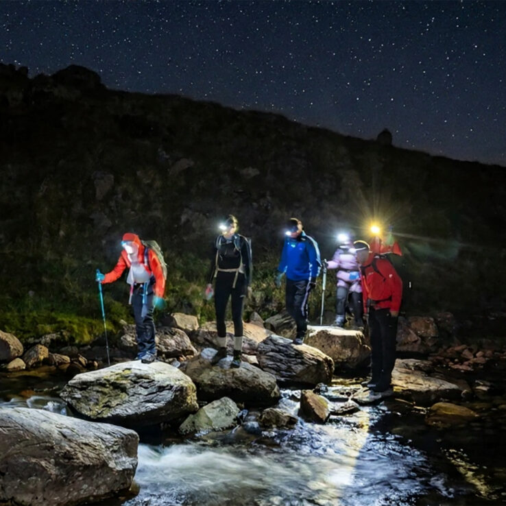 Team of hikers ascending Irish mountain peak at dawn with headtorches visible