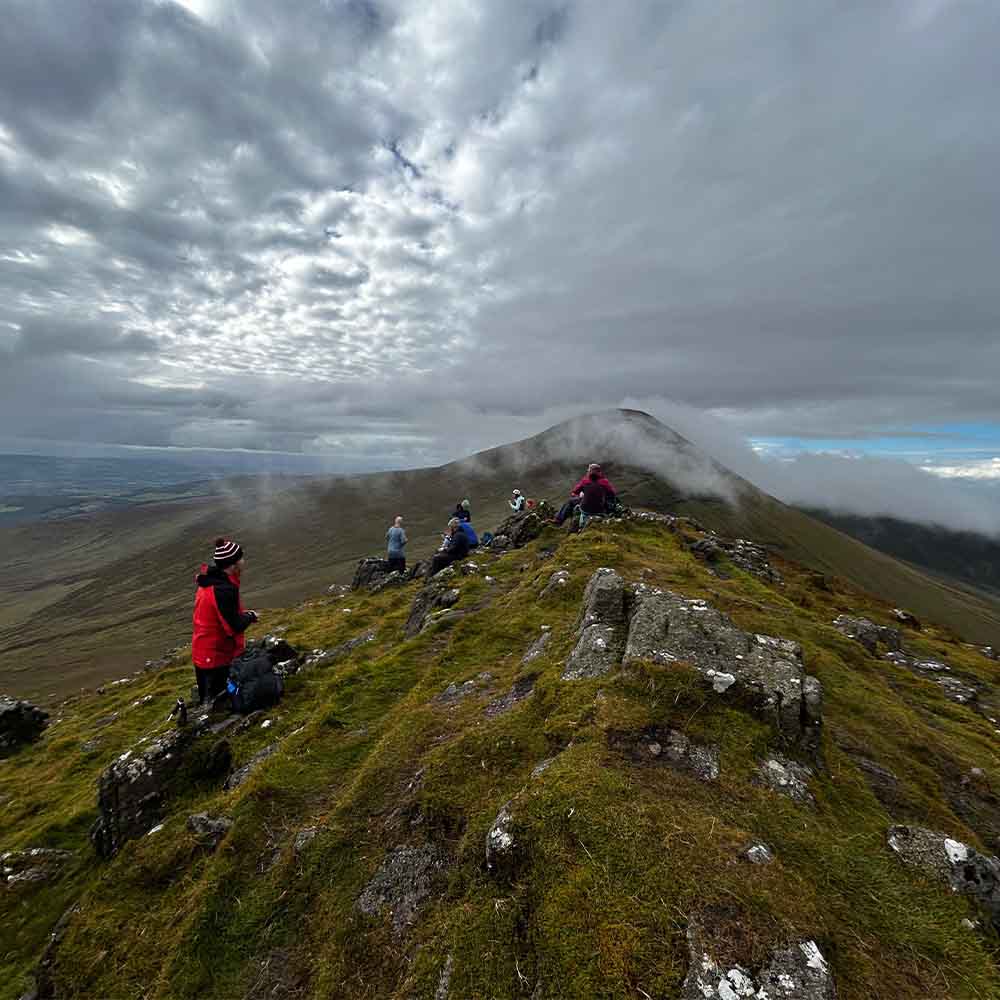 Tired hiker taking water break on Irish mountain ridge in summer heat
