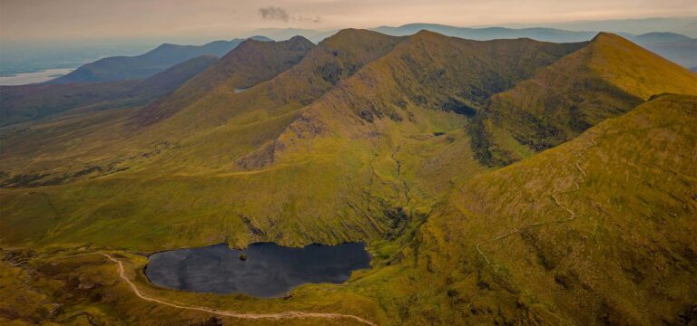 Hiker approaching MacGillycuddy Reeks at dawn, frost on grass, County Kerry Ireland