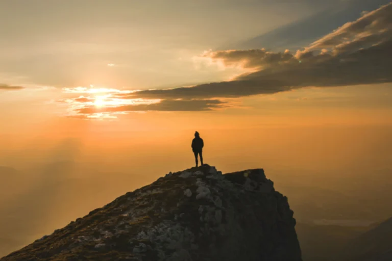 Trekker standing on the summit ridge of Mount Toubkal at dawn with High Atlas panorama