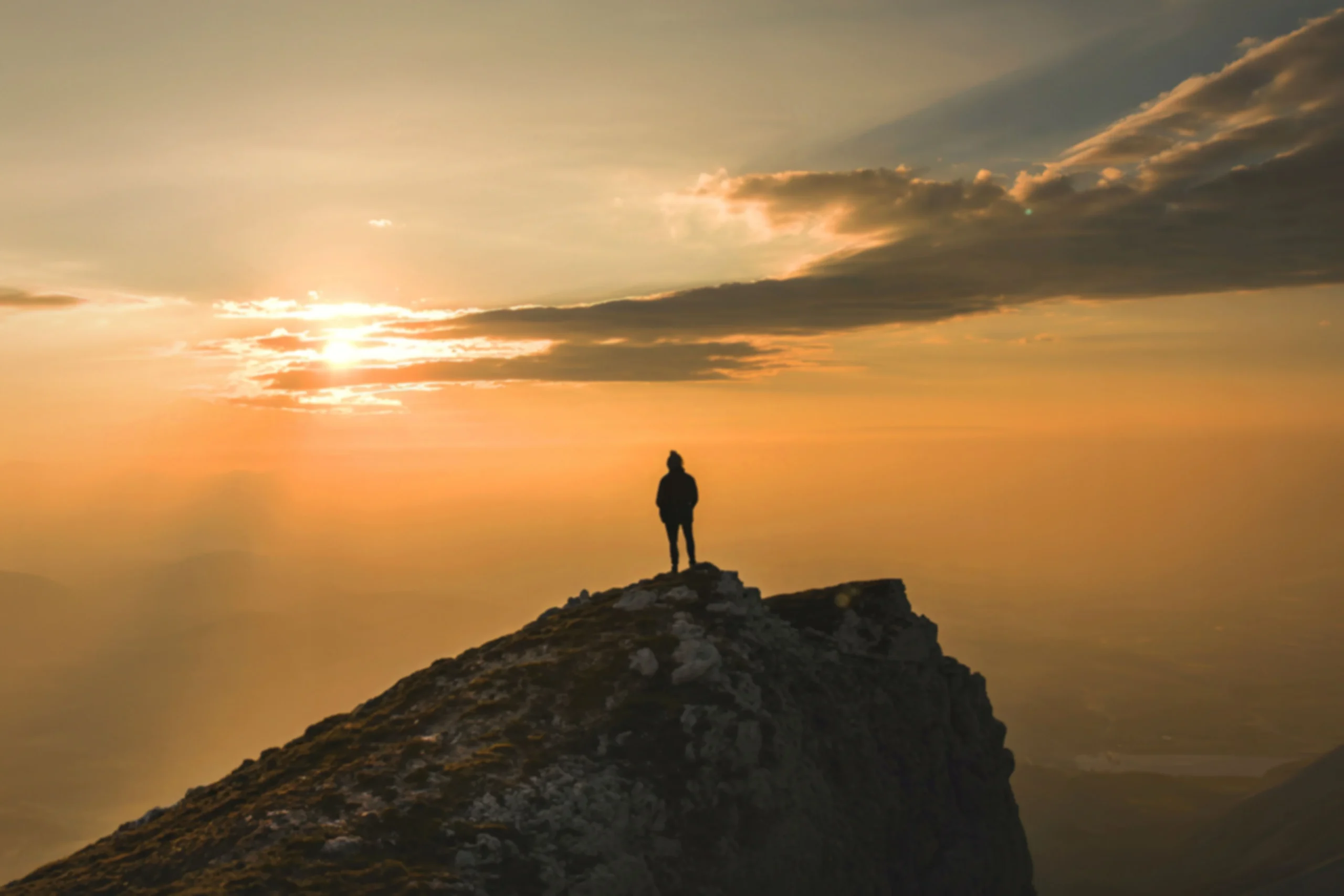 Trekker standing on the summit ridge of Mount Toubkal at dawn with High Atlas panorama