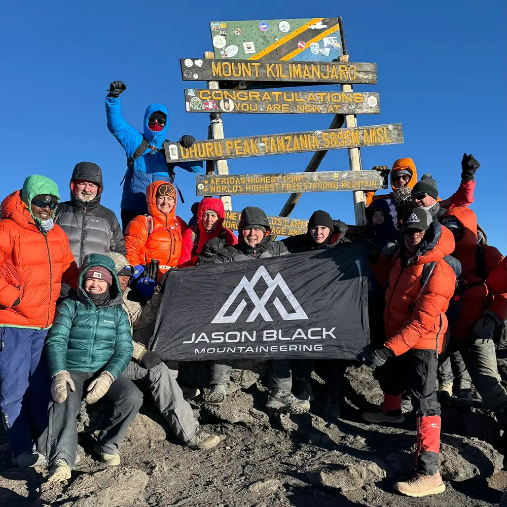 Mountaineer standing at Uhuru Peak summit sign Kilimanjaro 5895 metres Roof of Africa