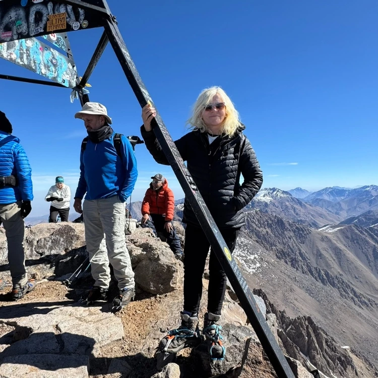 Female mountaineer standing at Mount Toubkal summit at 4,167m with High Atlas panorama at dawn