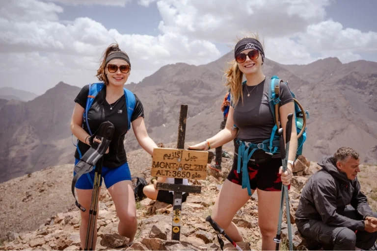 Female mountaineer standing at Mount Toubkal summit at 4,167m with High Atlas panorama at dawn