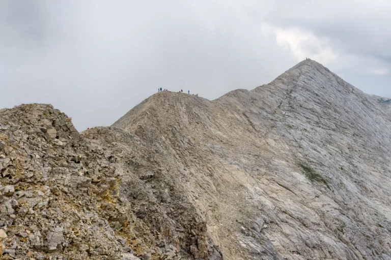 Hiker traversing Koncheto marble knife-edge ridge with fixed cables in Pirin Mountains Bulgaria