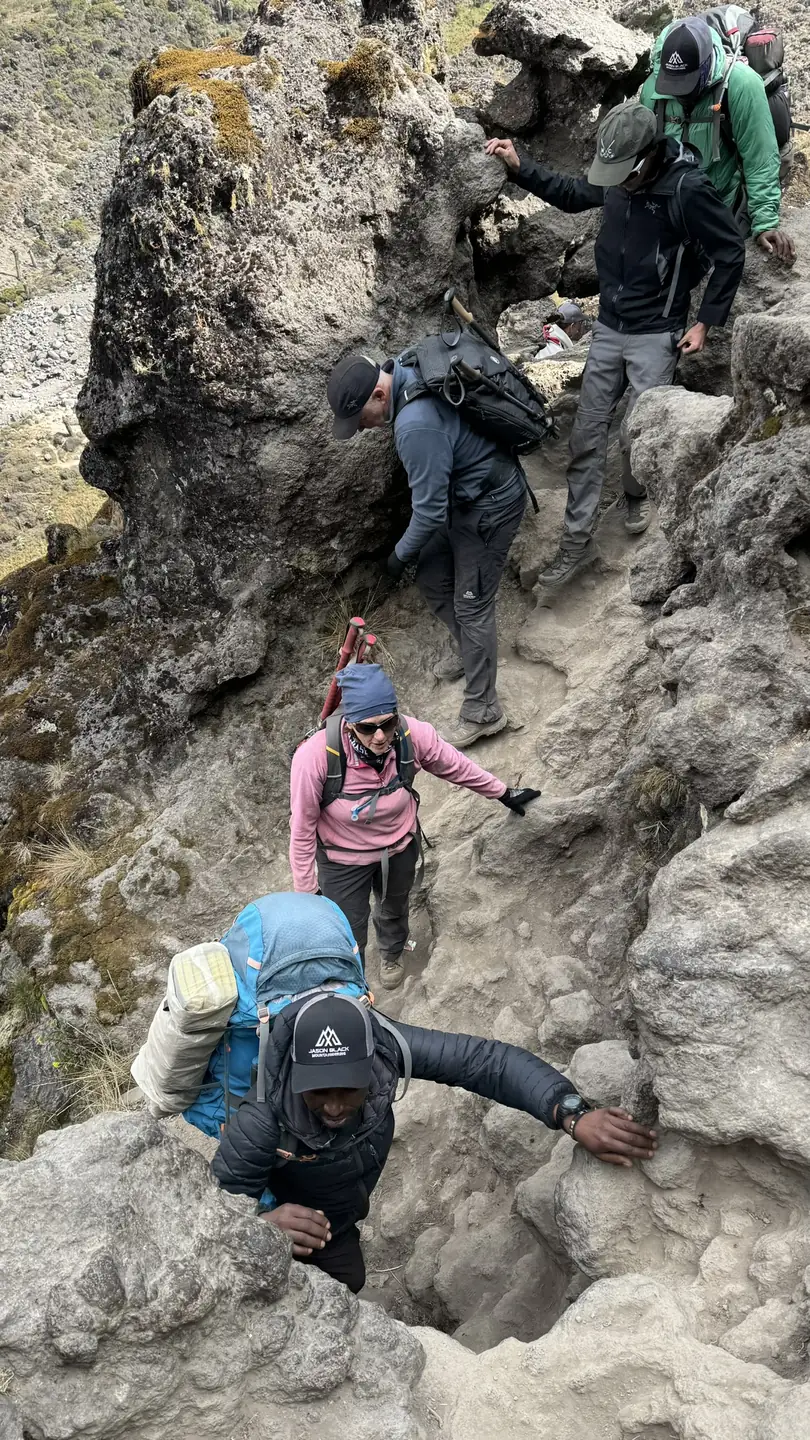 Climbers scrambling up the famous Barranco Wall on the Kilimanjaro Machame Whiskey Route using hands and feet on volcanic rock