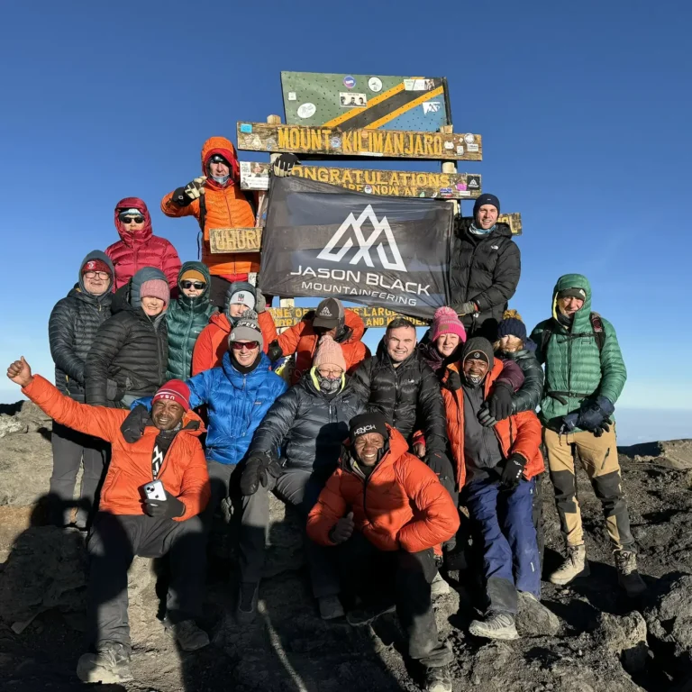 Black Mountaineering team at Uhuru Peak summit sign 5895 metres after completing Kilimanjaro Machame Whiskey Route seven day expedition
